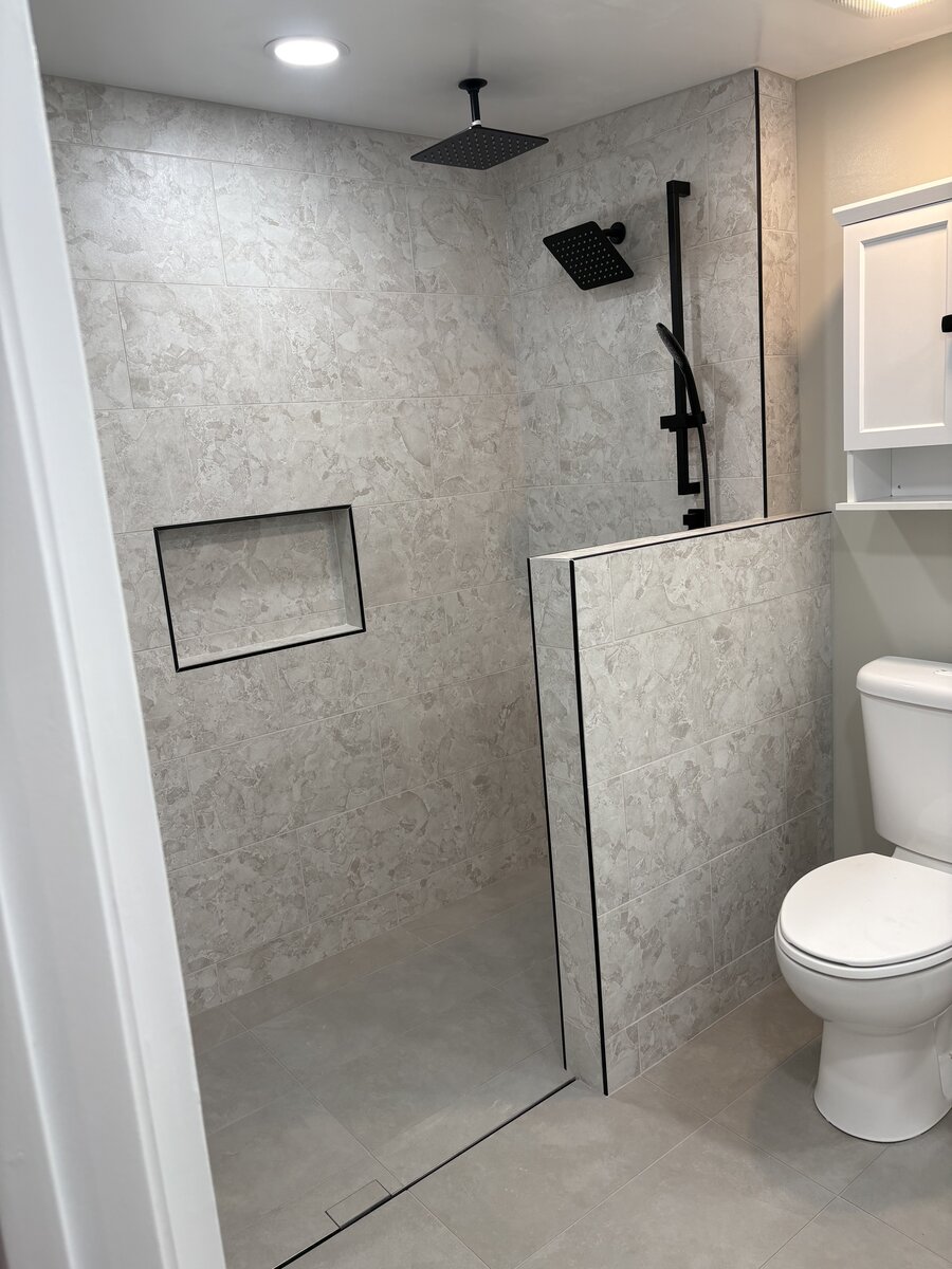 Walk-in shower with half wall, ceiling-mounted rain shower, and black fixtures